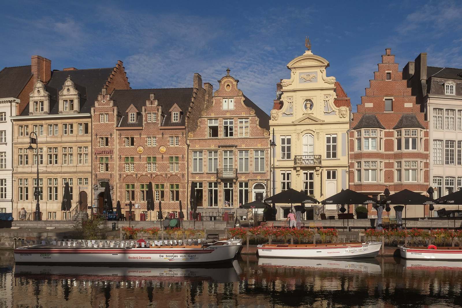Historische trap- en barokgevels aan de Korenlei in Gent, met terrassen, rondvaartboten en weerspiegelingen in de Leie