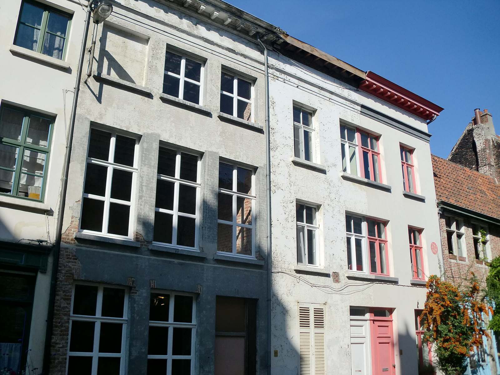 Oude rijhuizen met hoge ramen en grijze en witte gepleisterde gevels in de Abrahamstraat in Gent, onder een blauwe lucht